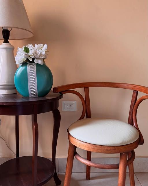 Silla de madera curvada con asiento tapizado en blanco, junto a una mesa con flores